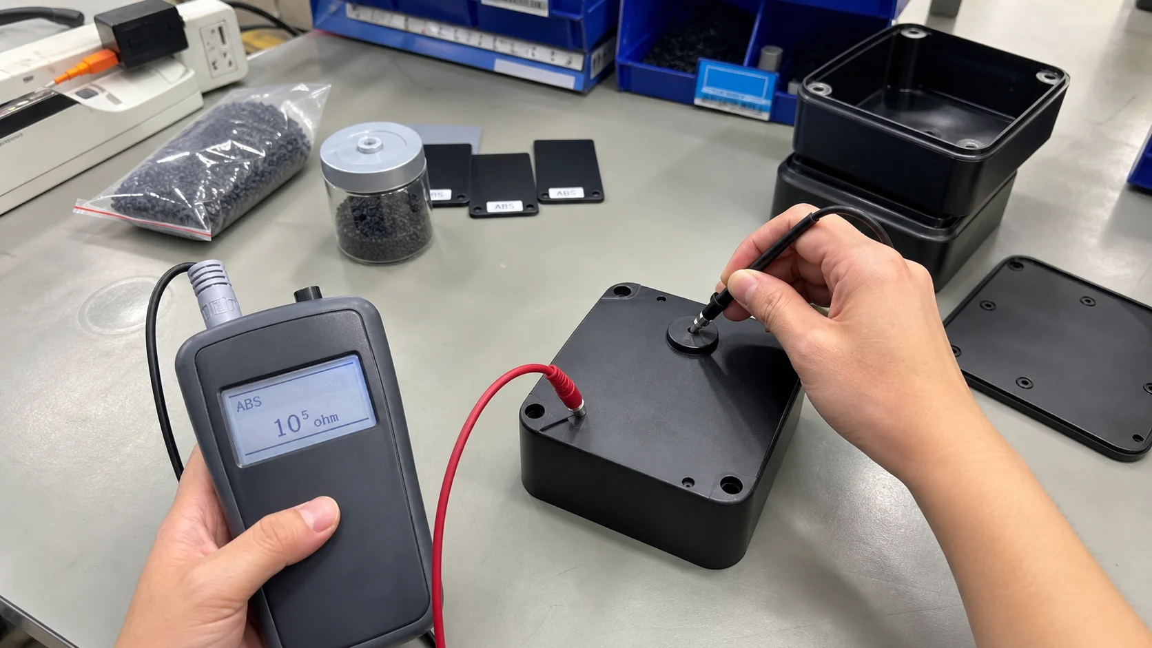 Real smartphone-style surface resistance test on black conductive ABS housings and covers in an electronics QA area