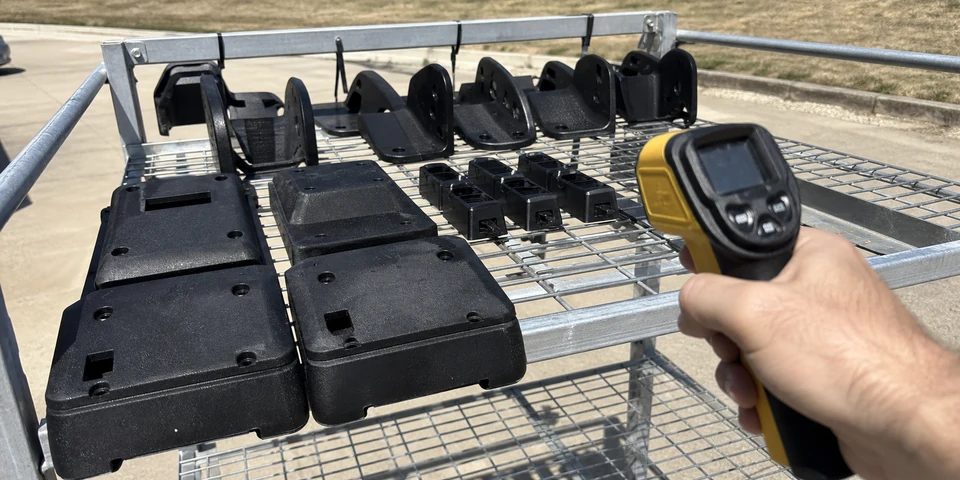 Outdoor validation rack with black polypropylene molded parts under sunlight and handheld thermal inspection